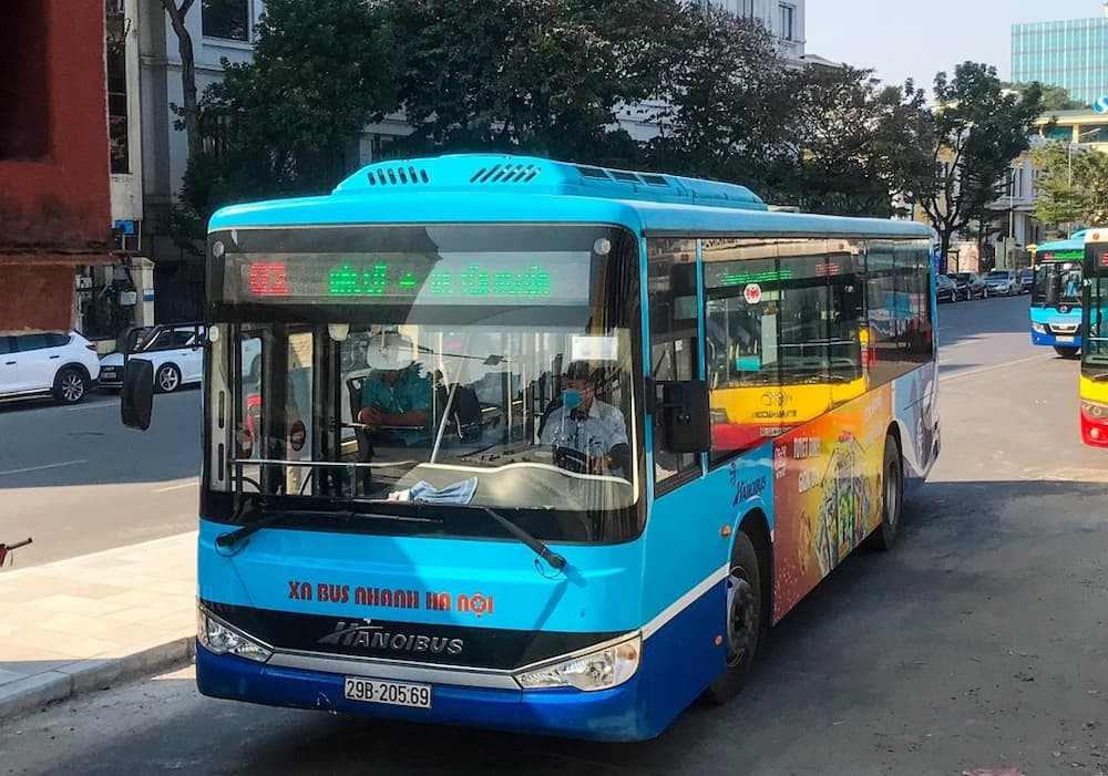 Một chiếc xe buýt màu xanh đang di chuyển trên đường phố Hà Nội
