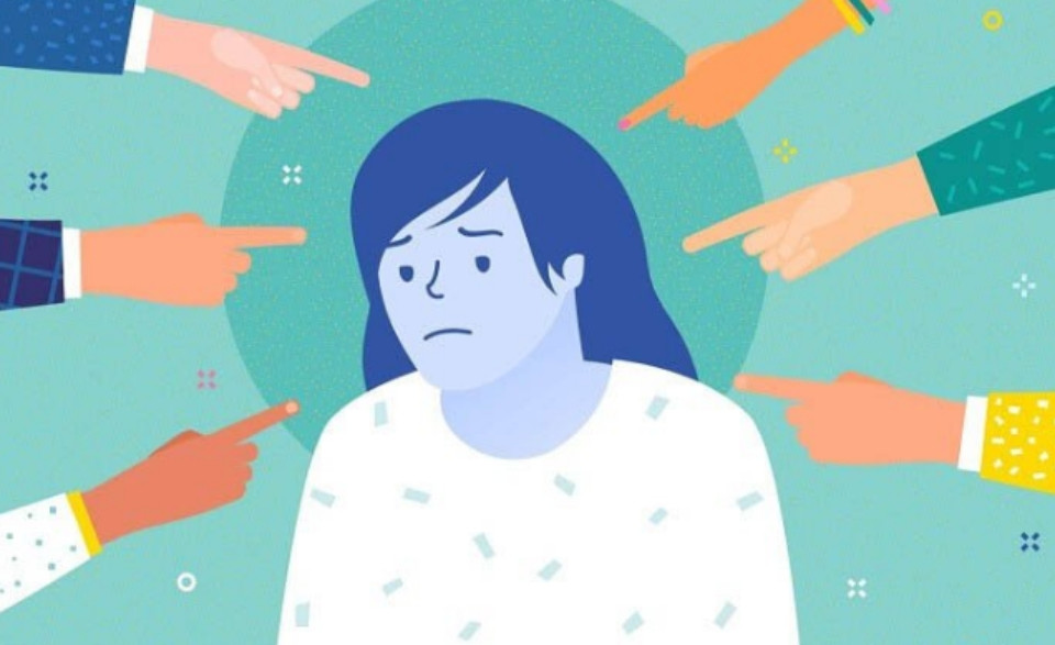 Một người phụ nữ ngồi trên ghế với vẻ mặt trầm tư, tay ôm đầu gối, thể hiện sự suy nghĩ tiêu cực