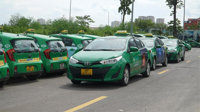 Một chiếc taxi Mai Linh màu xanh lá cây đang di chuyển trên đường phố Cà Mau, thể hiện sự quen thuộc của thương hiệu này
